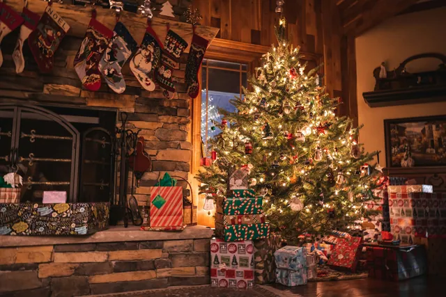 Christmas tree with lights next to a fireplace with stockings