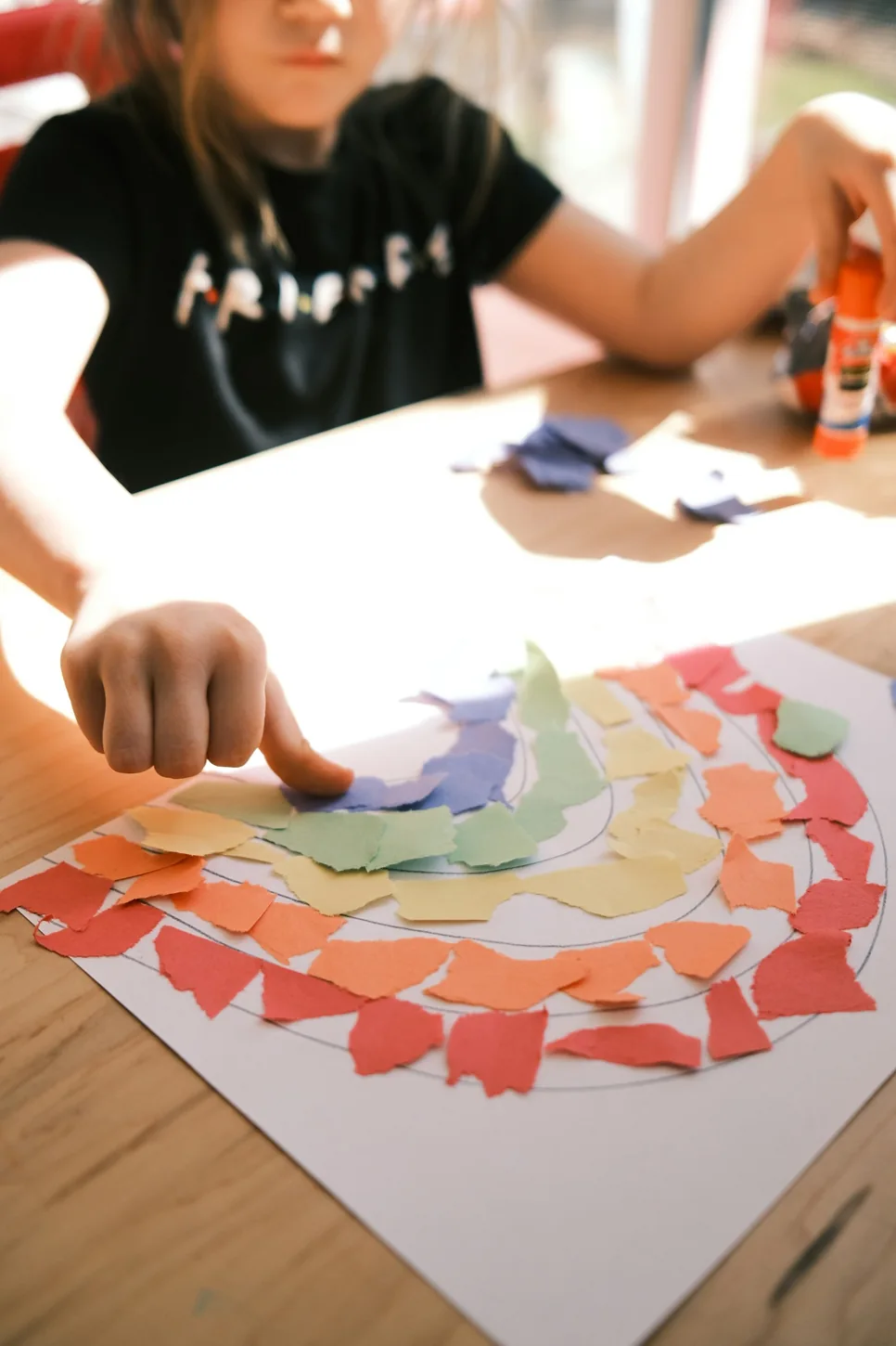 Child making a colourful paper craft at a wooden table